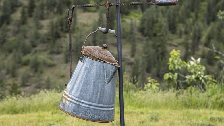 old fashioned coffee pot hanging on an iron hook outdoors