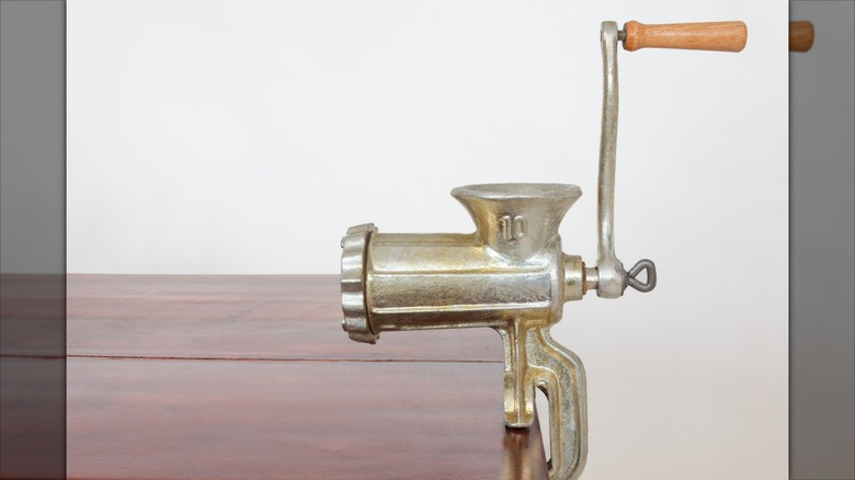 A vintage meat grinder clamped to a wood table