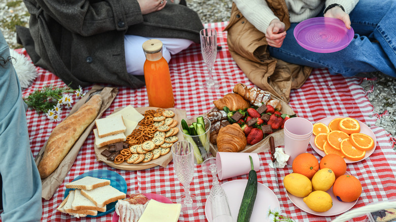 People at a picnic with fruit, drinks, bread, and snacks