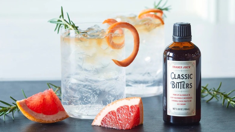 A bottle of Trader Joe's Classic Bitters on a table next to two cocktails