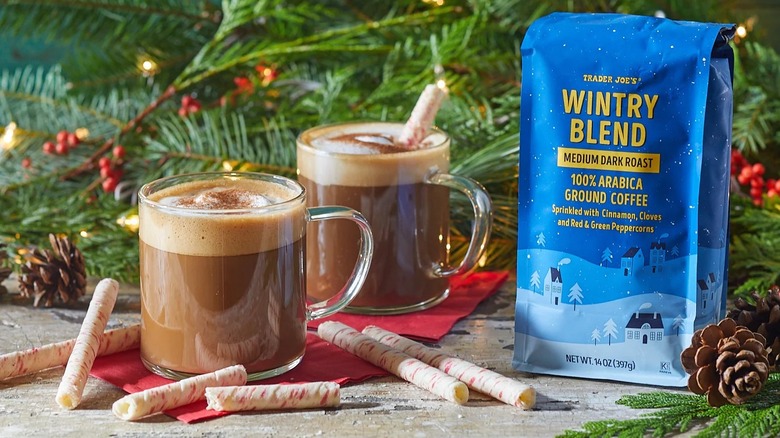 A bag of Trader Joe's Wintry Blend coffee on a table next to two glass mugs of coffee and surrounded by evergreen boughs
