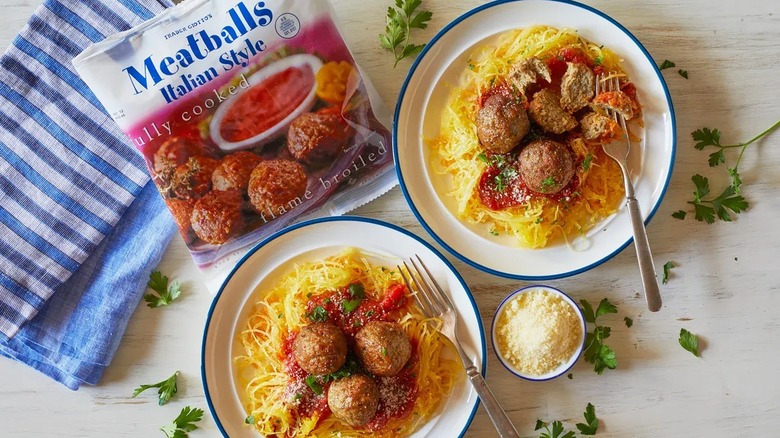 Bag of Trader Joe's Italian meatballs next to two plates of spaghetti and meatballs