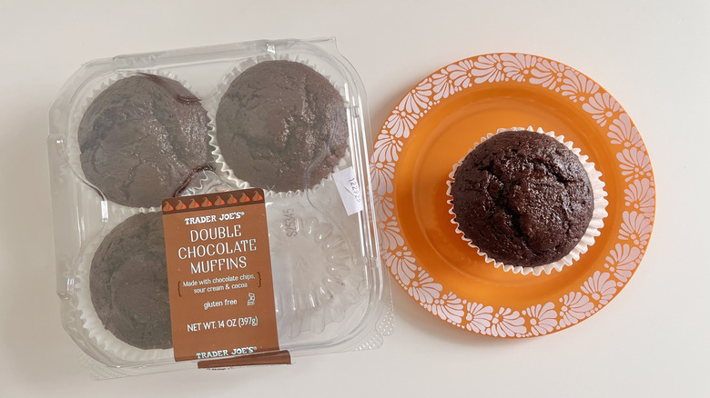 Chocolate muffin on a plate with a plastic container with three Trader Joe's Gluten Free Double Chocolate Muffins