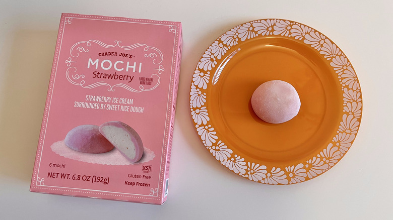 Top view of a box of Strawberry Mochi next to a plate with one mochi