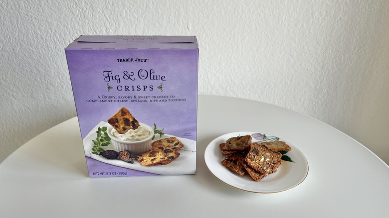 Cardboard box of fig and olive crisps next to a small plate of them on a white table