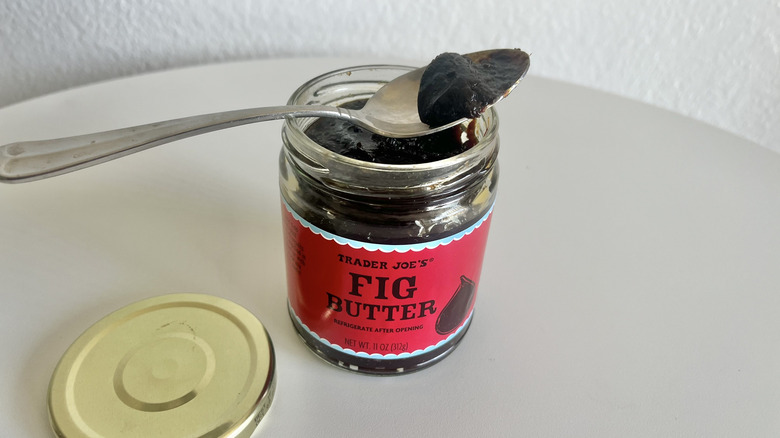 An open jar of fig butter on table with a spoon on top