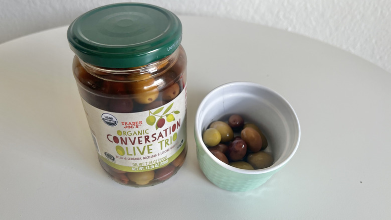 A jar of Olive Trio with a ramekin of green and dark olives