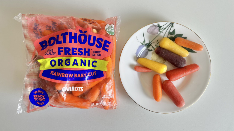 Rainbow baby carrots in plastic baggie next to a plate of baby carrots