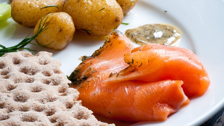 Gravad laks with crispbread and potatoes on a white plate
