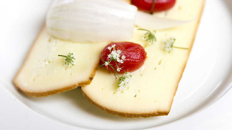 Smoked cheese from Denmark on a white plate with tomato and floral garnishes