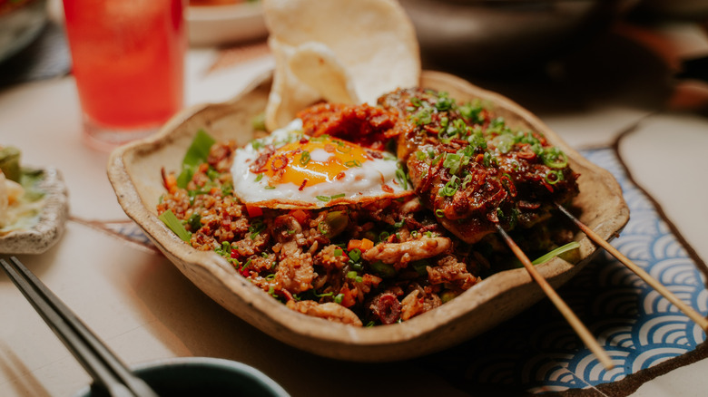 Plate of nasi goreng with meat skewers and fried egg on top