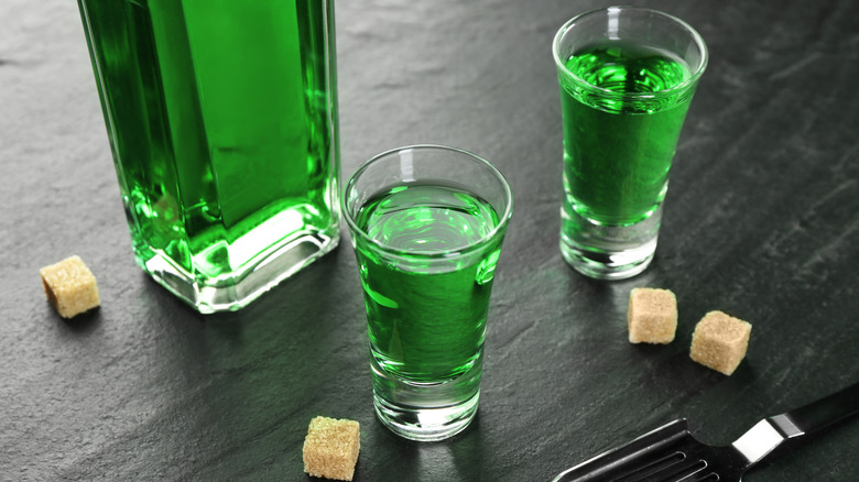 Bottle and glasses of absinthe and sugar cubes on black table