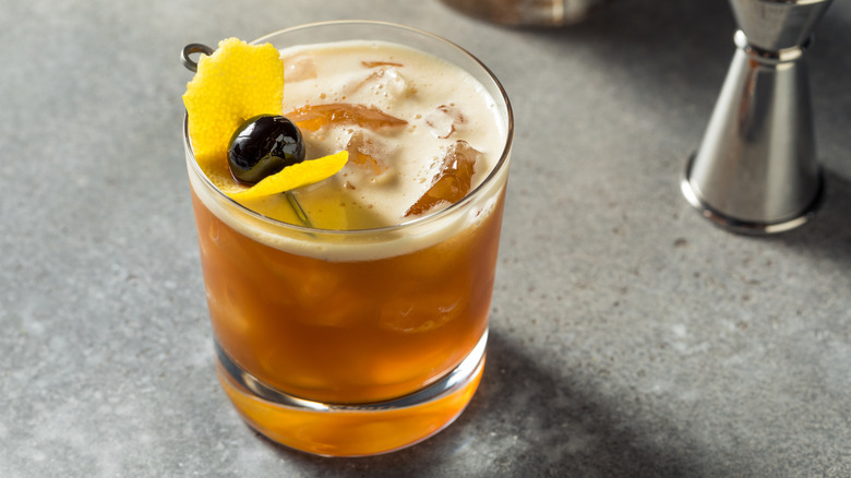 Amaro sour with lemon peel and olive garnish on a gray counter