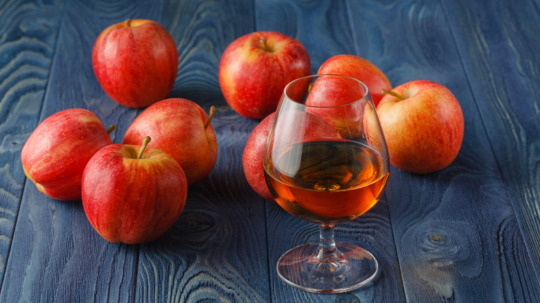 Glass of Calvados next to several red apples on a blue table