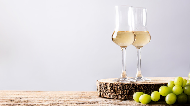 Two glasses of grappa on wooden table and board with green grapes