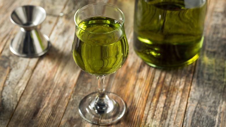Green Chartreuse in glass with bottle on wooden table