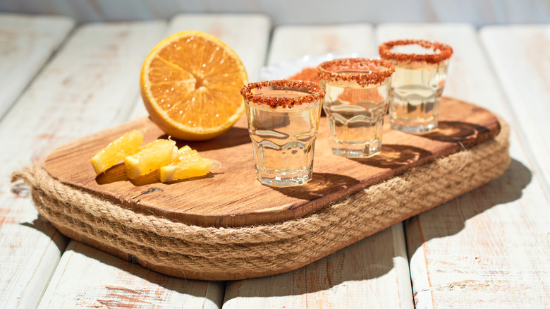 Three shots of mezcal on wooden board with orange half and orange wedges