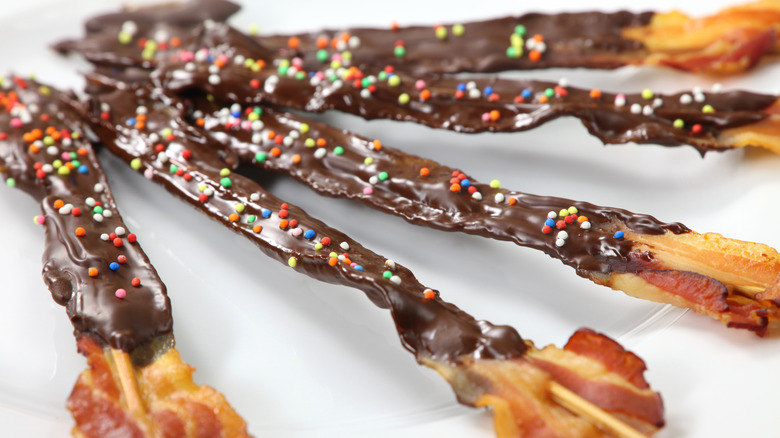 Crispy cooked bacon on a stick dipped in dark chocolate and drizzled with sprinkles.