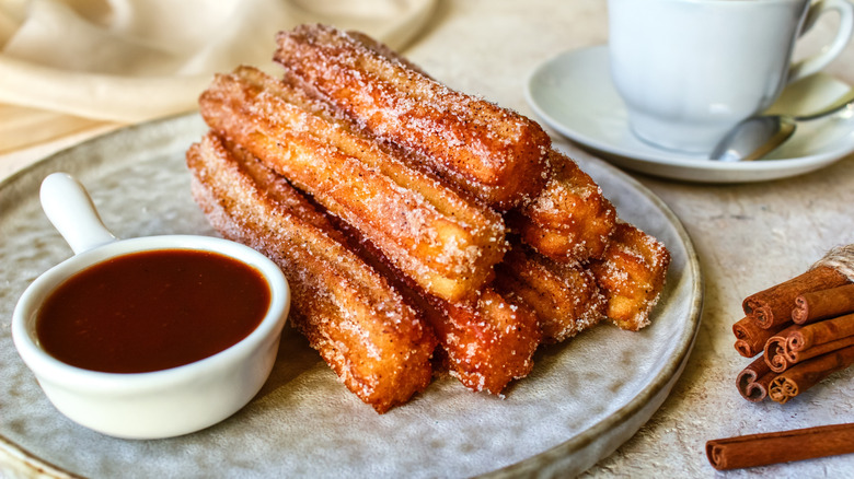 Cinnamon churros on a plate with a side of chocolate sauce.