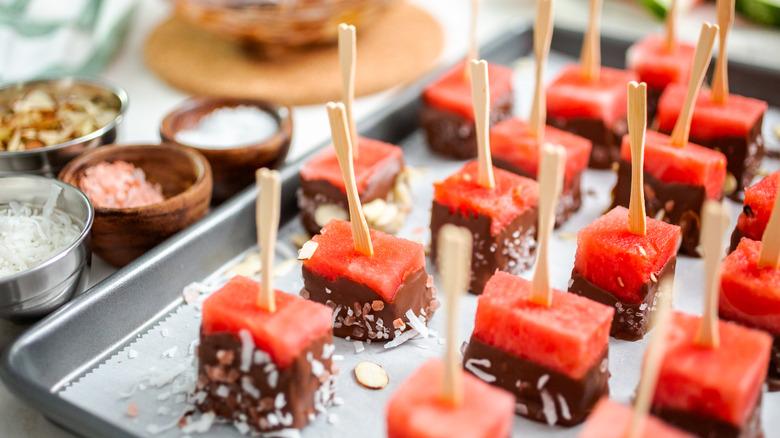 Cubed cut watermelon on a stick dipped in chocolate and coated with sea salt and almonds.