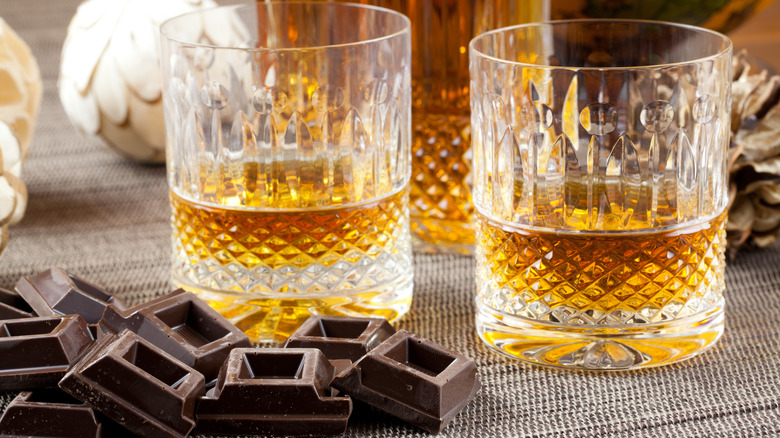 Two glasses filled with whiskey and many bites of chocolate sitting next to the glasses.