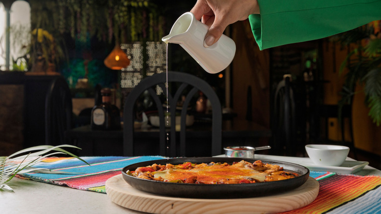 Someone pouring a liquid over a dish of queso fundido