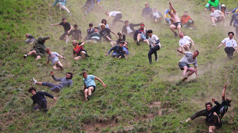 Dozens of people tumble down a dusty, grassy hill during the Gloucestershire Cheese Rolling Event