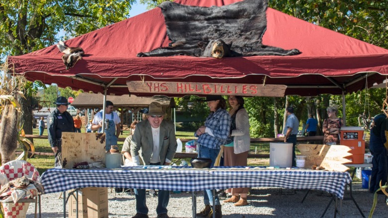 People standing behind behind a table under a tent with a bearskin on it at an outdoor festival