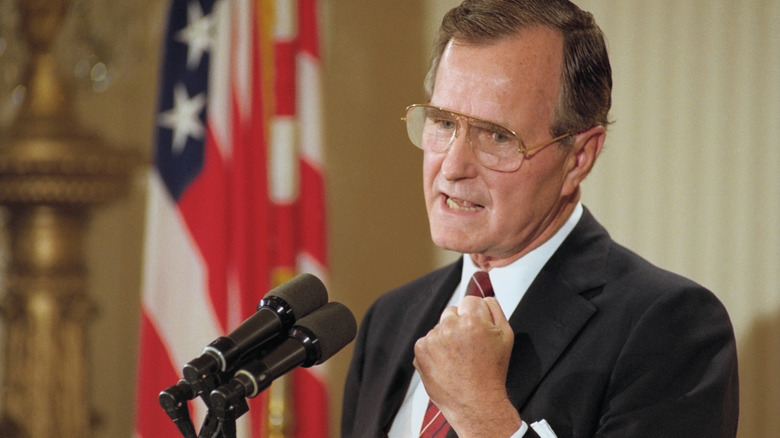 George H. W. Bush speaking into microphone with American flag in the background