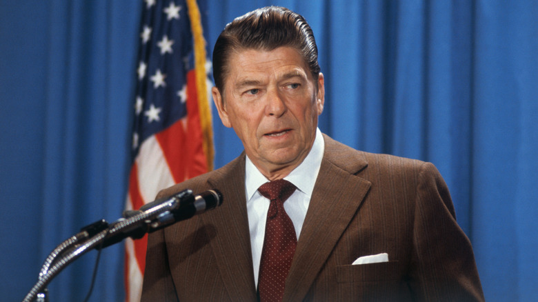 Ronald Reagan speaking into microphone in front of American flag