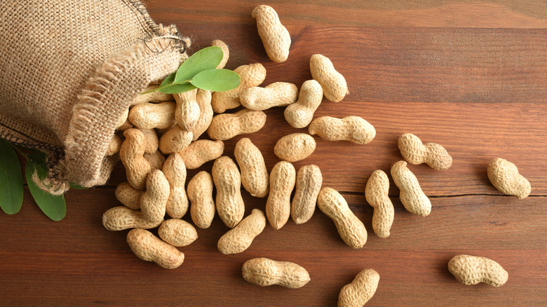 unshelled peanuts pouring out of a burlap bag on a wooden table