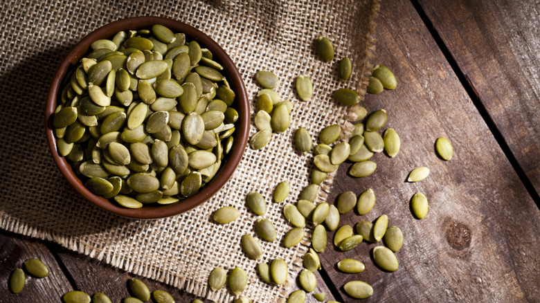 Pumpkin seeds in a bowl and spread around the bowl