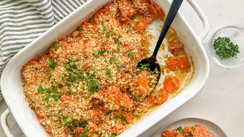 Breadcrumb-topped carrot casserole in white baking dish with spoon