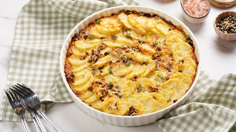 Casserole topped with sliced potatoes and black peppercorns in round white dish