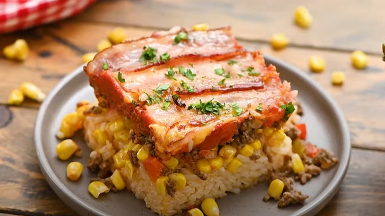Portion of seven layer casserole with bacon, corn, and rice on plate