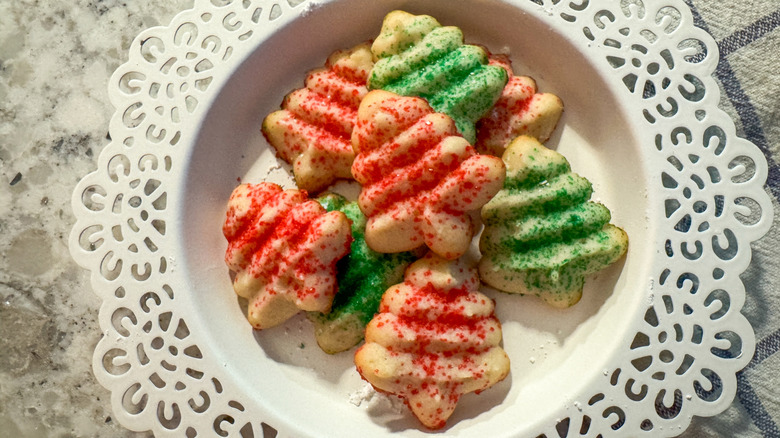 A round platter of Christmas spritz cookies with red and green sprinkles in a white bowl with white doily