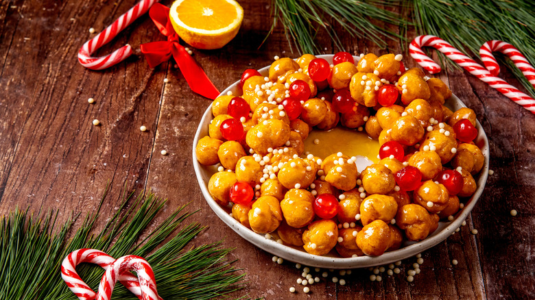 Struffoli with maraschino cherries and white sprinkles surrounded by pine needles and candy canes