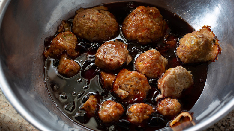 A close up of tiny meatballs with a grape jelly sauce in a metal bowl