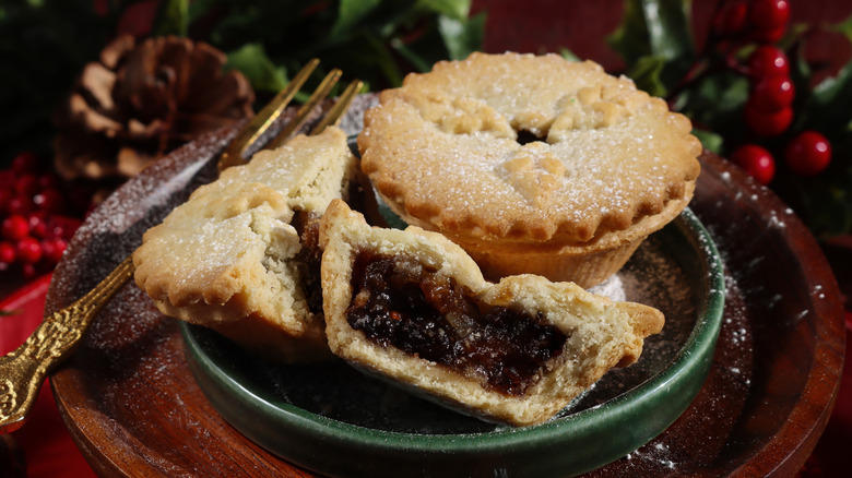 Two small mince pies, one broken in half, on a green plate in front of a Christmas background