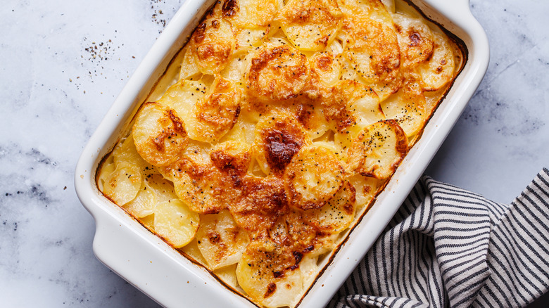 Cheesy potatoes au gratin in a white casserole dish on a marble counter