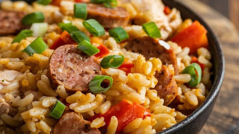 A black bowl of Jambalaya  with sausage, peppers, and green onions