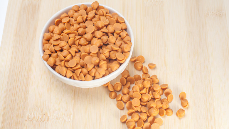 Butterscotch chips in a white bowl on wooden background.