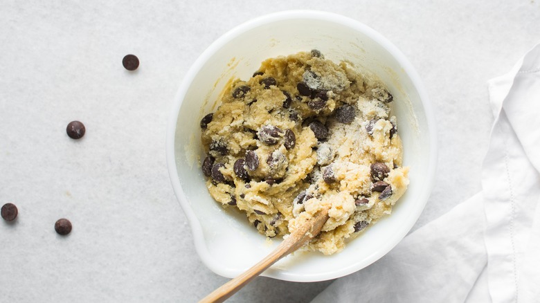 A white bowl of chocolate chip cookie dough on white background.