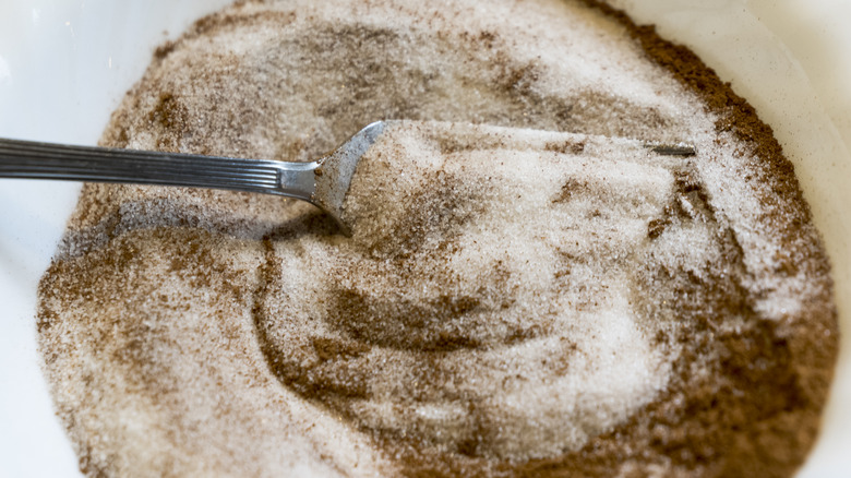 Cinnamon and sugar being stirred with a spoon in a white dish.