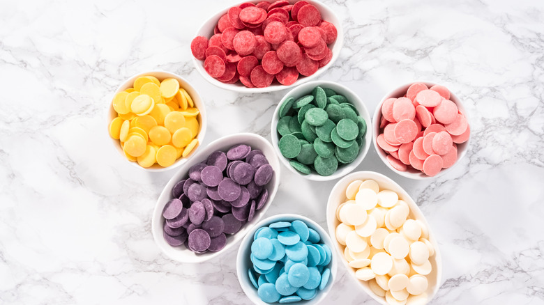 A variety of candy melts in white bowls on marble counter.