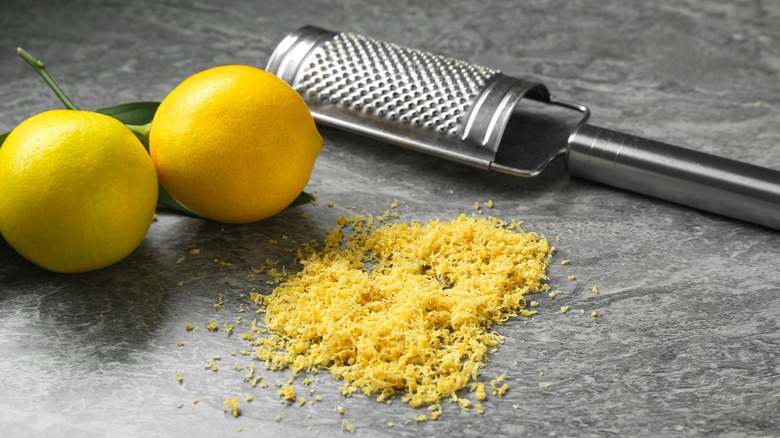 Lemons, lemon zest, and zester on gray marble background.