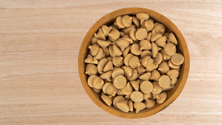 Peanut butter chips in a wooden bowl on wooden background.