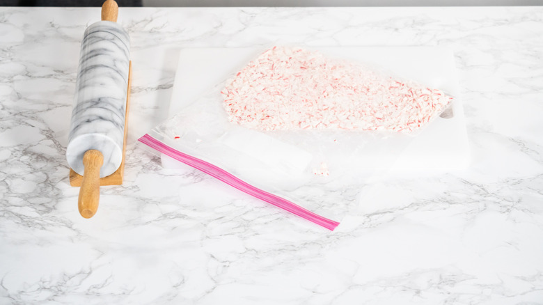 Rolling pin and peppermint pieces in a plastic bag on marble counter.
