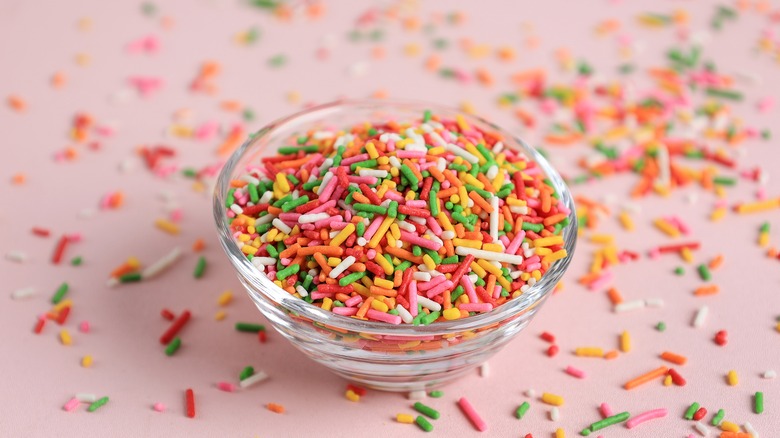 Rainbow sprinkles in glass bowl on a pink background.