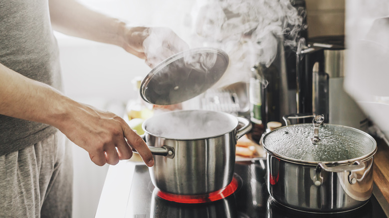 Person lifting the lid off a pot on the stove, releasing steam into the room